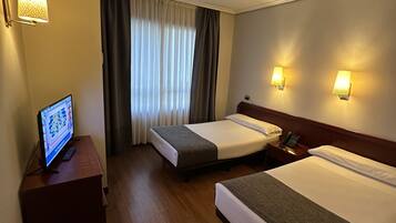 Habitación de hotel con dos camas, un escritorio con computadora, teléfono y ventana con cortinas.