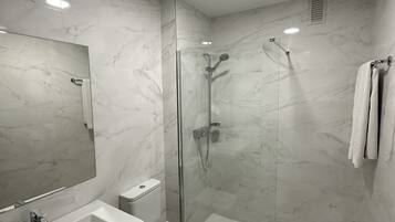 Ein modernes Badezimmer mit Marmorboden, einer in Glas eingefassten Dusche, einem weißen Waschbecken und einem großen Spiegel.