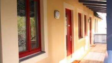 Un corridoio con finestre e porte incorniciate di rosso, che conduce a un portico coperto.