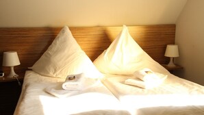 Une chambre d’hôtel avec une tête de lit en bois, deux oreillers, un lit bien fait avec une serviette blanche, et une table de chevet avec une lampe.