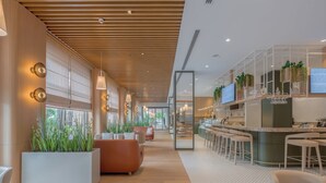 Een moderne hotellobby met een houten plafond, zithoeken, een bar en kamerplanten.