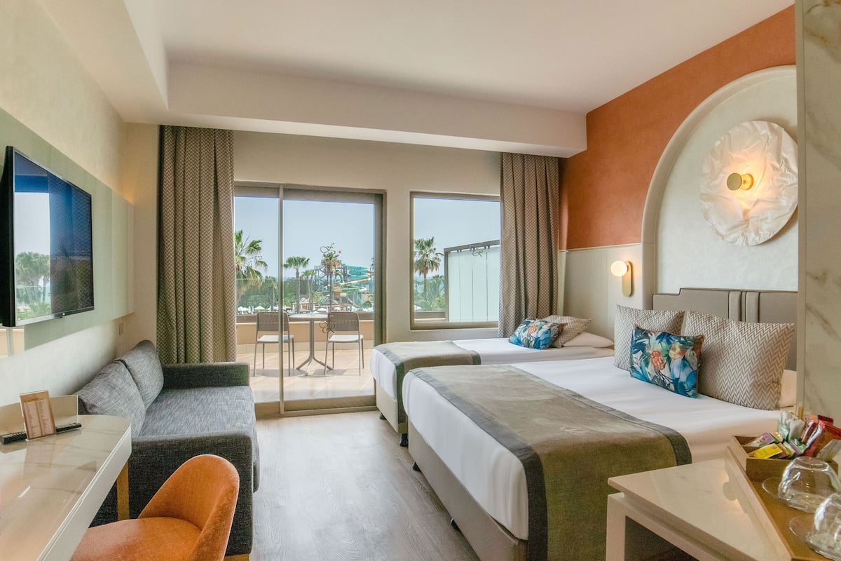 Quarto de hotel com duas camas, um sofá, uma escrivaninha e uma televisão.