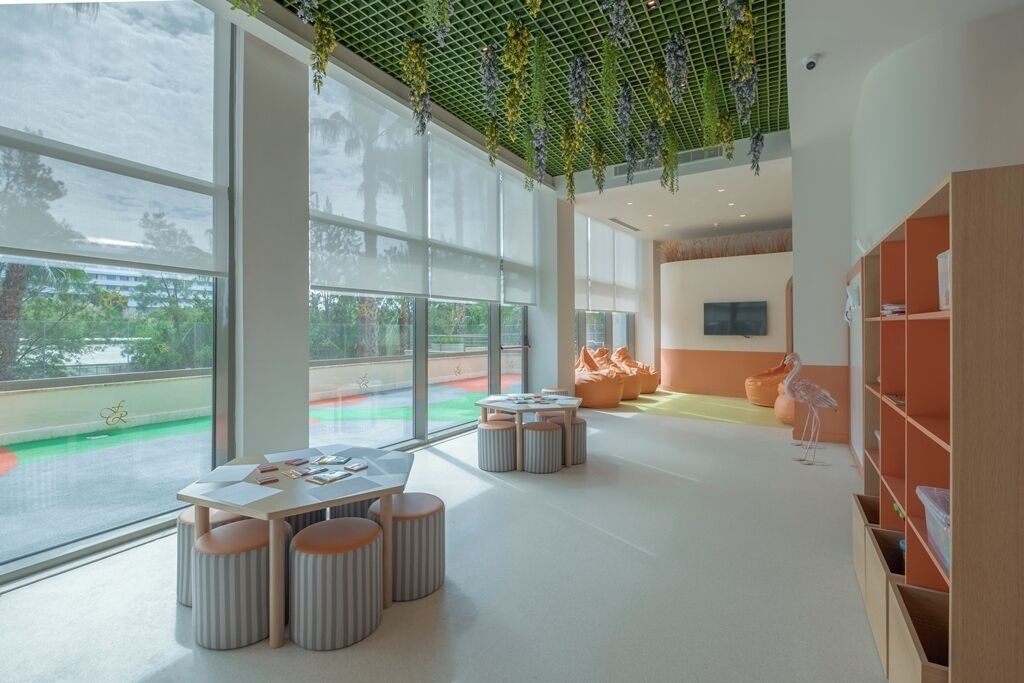 A spacious indoor area with large windows, a ceiling garden, and a seating area with tables and ottomans.