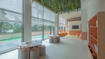 A spacious indoor area with large windows, a ceiling garden, and a seating area with tables and ottomans.