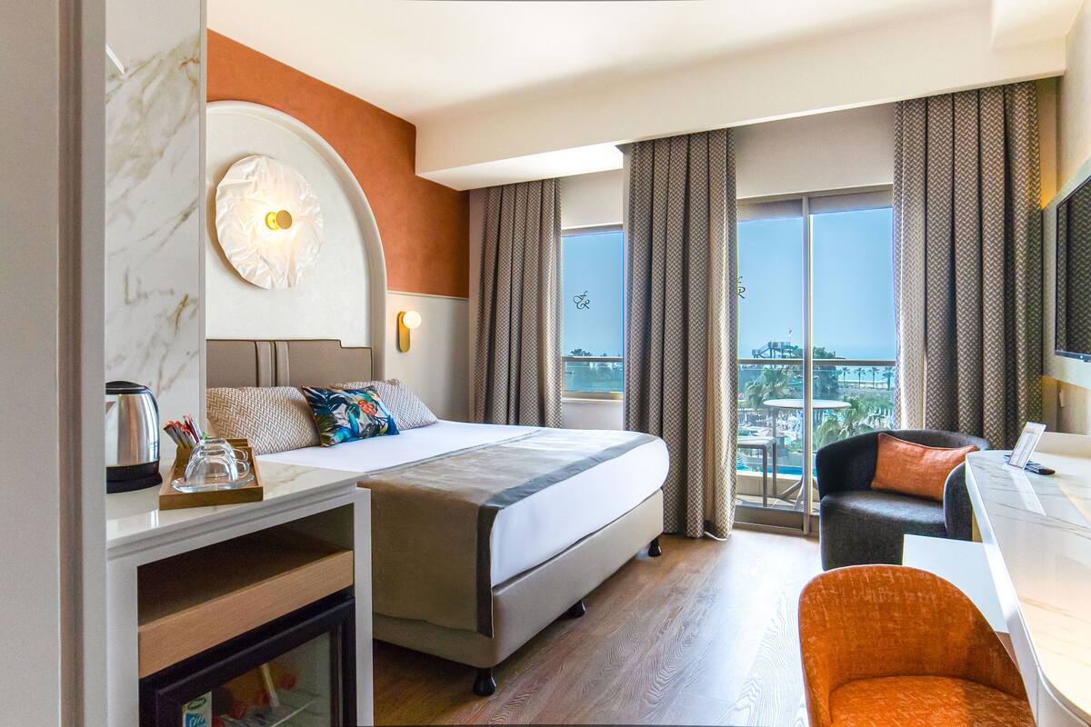 Quarto de hotel com cama, escrivaninha, cadeira e vista para a cidade.