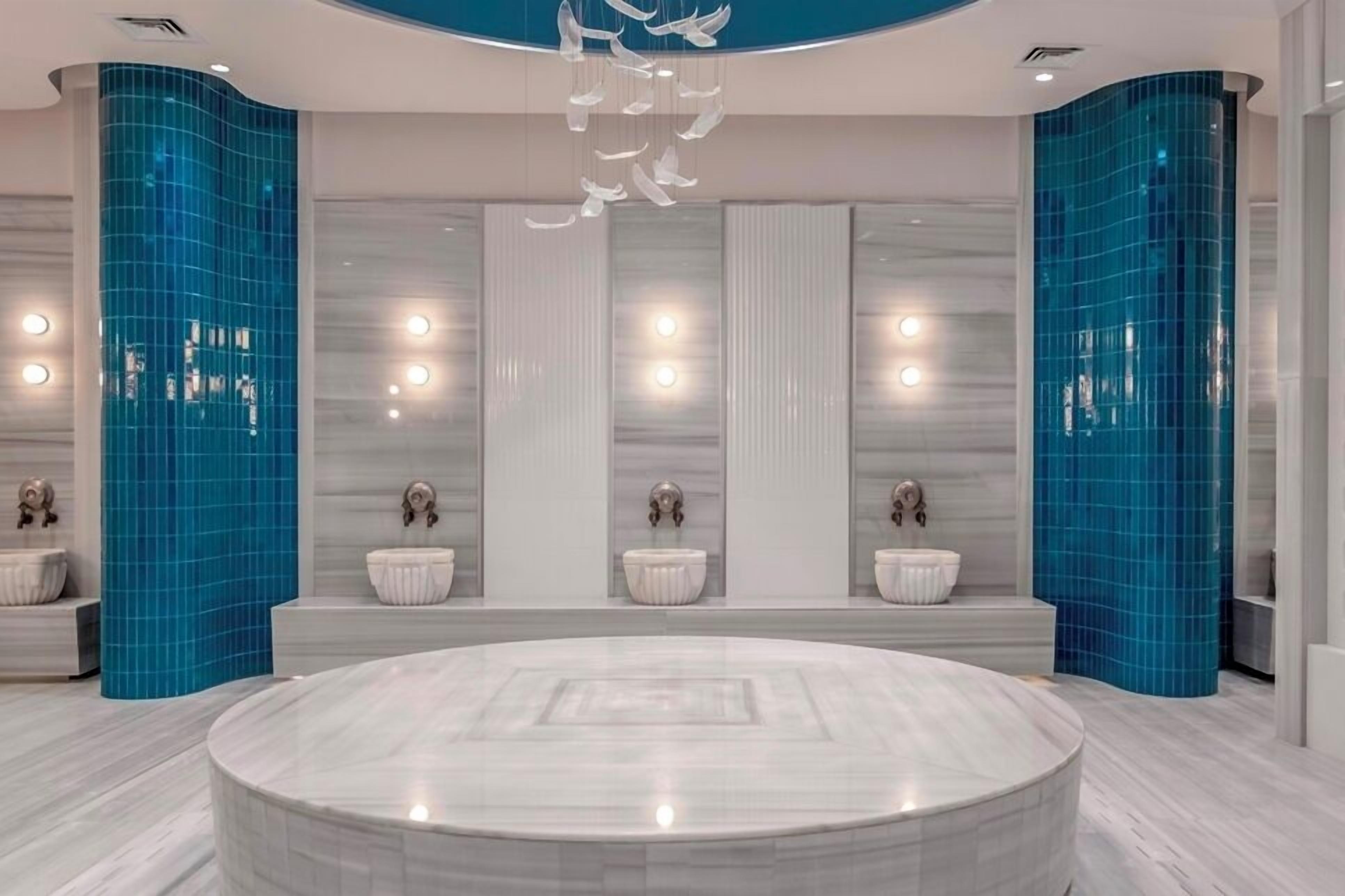 Un baño moderno con un lavamanos central de mármol, paredes con azulejos azules y una lámpara decorativa en el techo.
