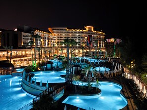 A hotel with multiple swimming pools, palm trees, and a well-lit facade at night. - Fame Residence Lara & Spa - All Inclusive (Antalya)
