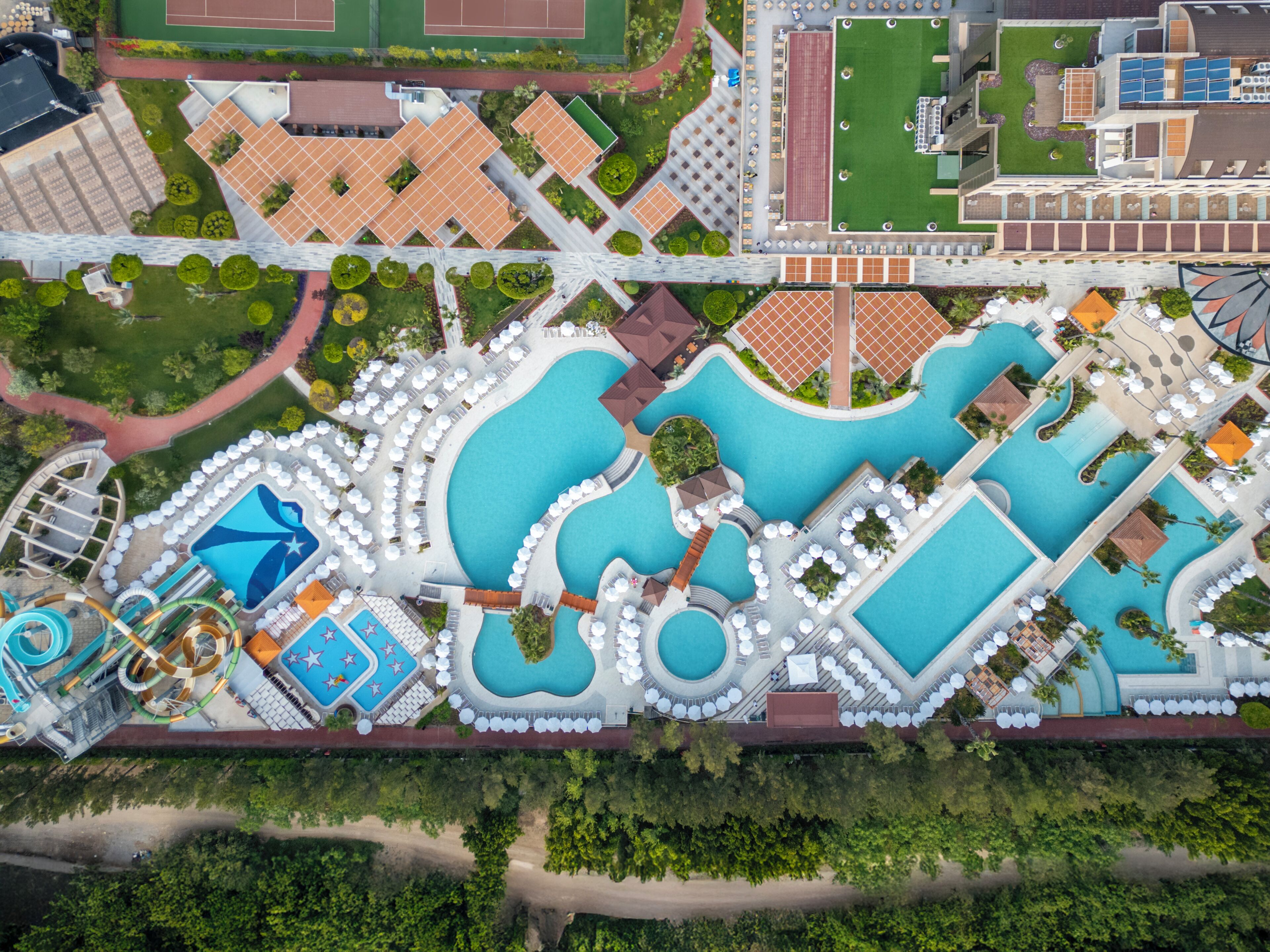 Luchtbeeld van een resort met diverse zwembaden, een waterpark en een tennisbaan.