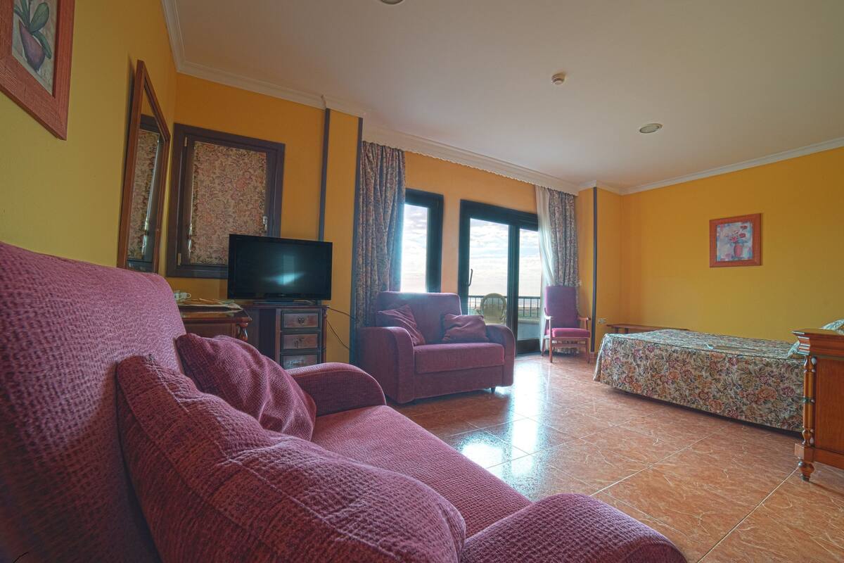 Una sala de estar con un sofá, televisión, una silla y una cama.