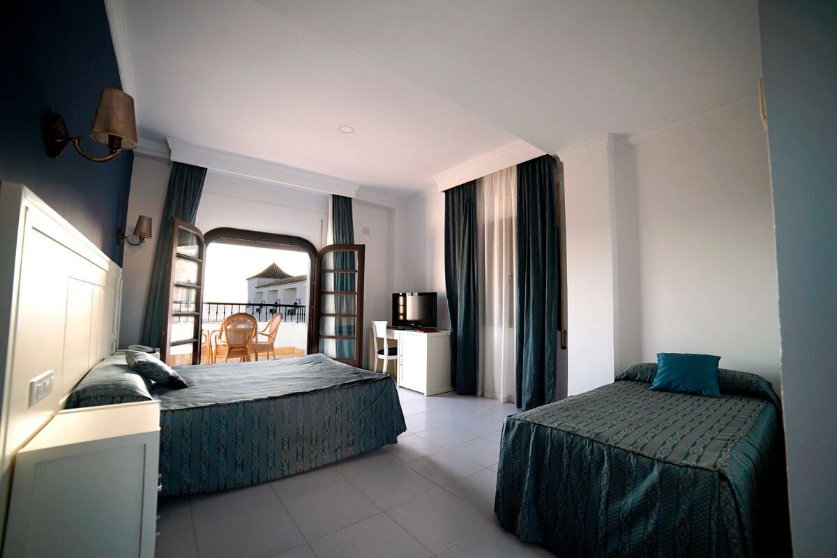 Habitación de hotel con dos camas, un escritorio, una silla y un televisor.