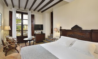 Habitación de hotel con una cama, televisión, escritorio con lámpara, una silla y vistas al exterior a través de una ventana.