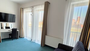 Ett hotellrum med en stor säng, ett skrivbord, en stol, en platt-TV och stora fönster med gardiner.