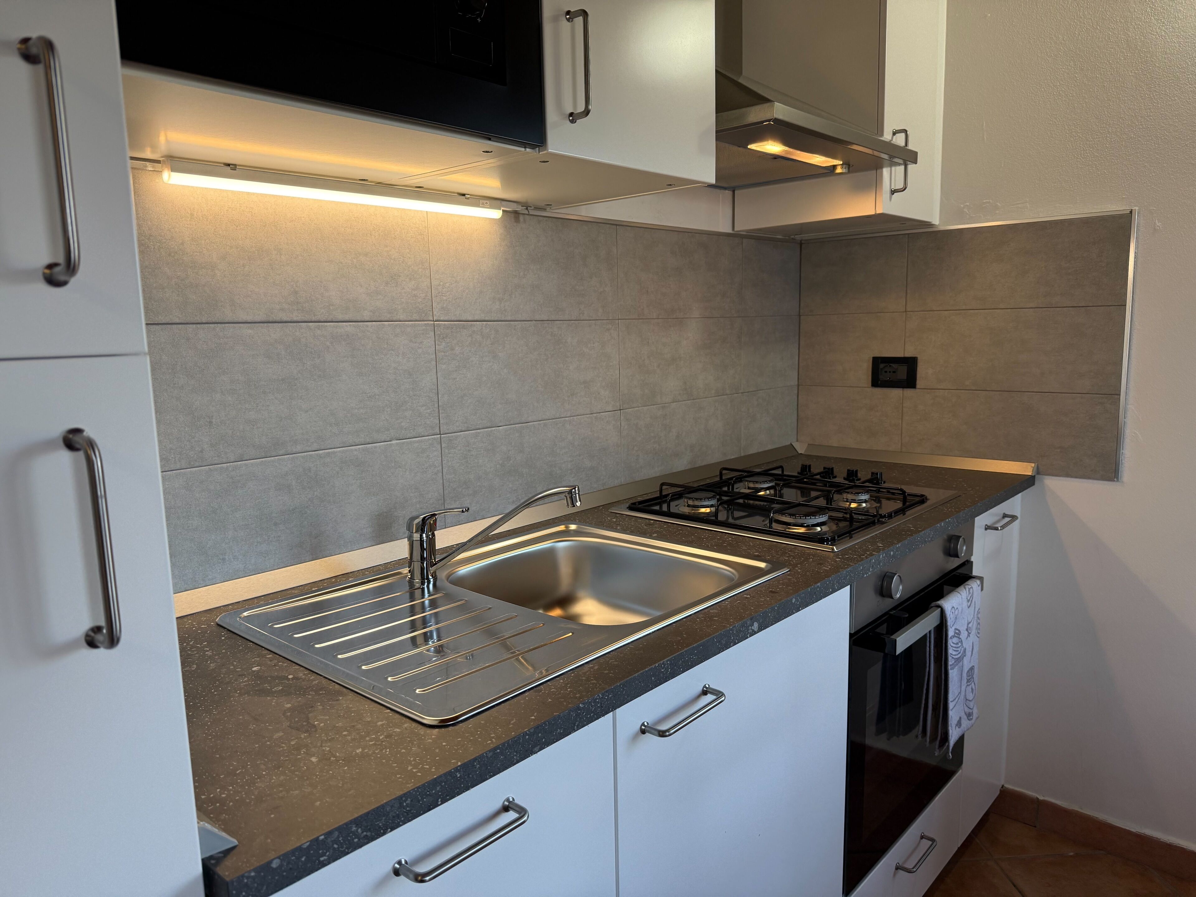 A modern kitchen with a gas stove, stainless steel sink, and white cabinetry.