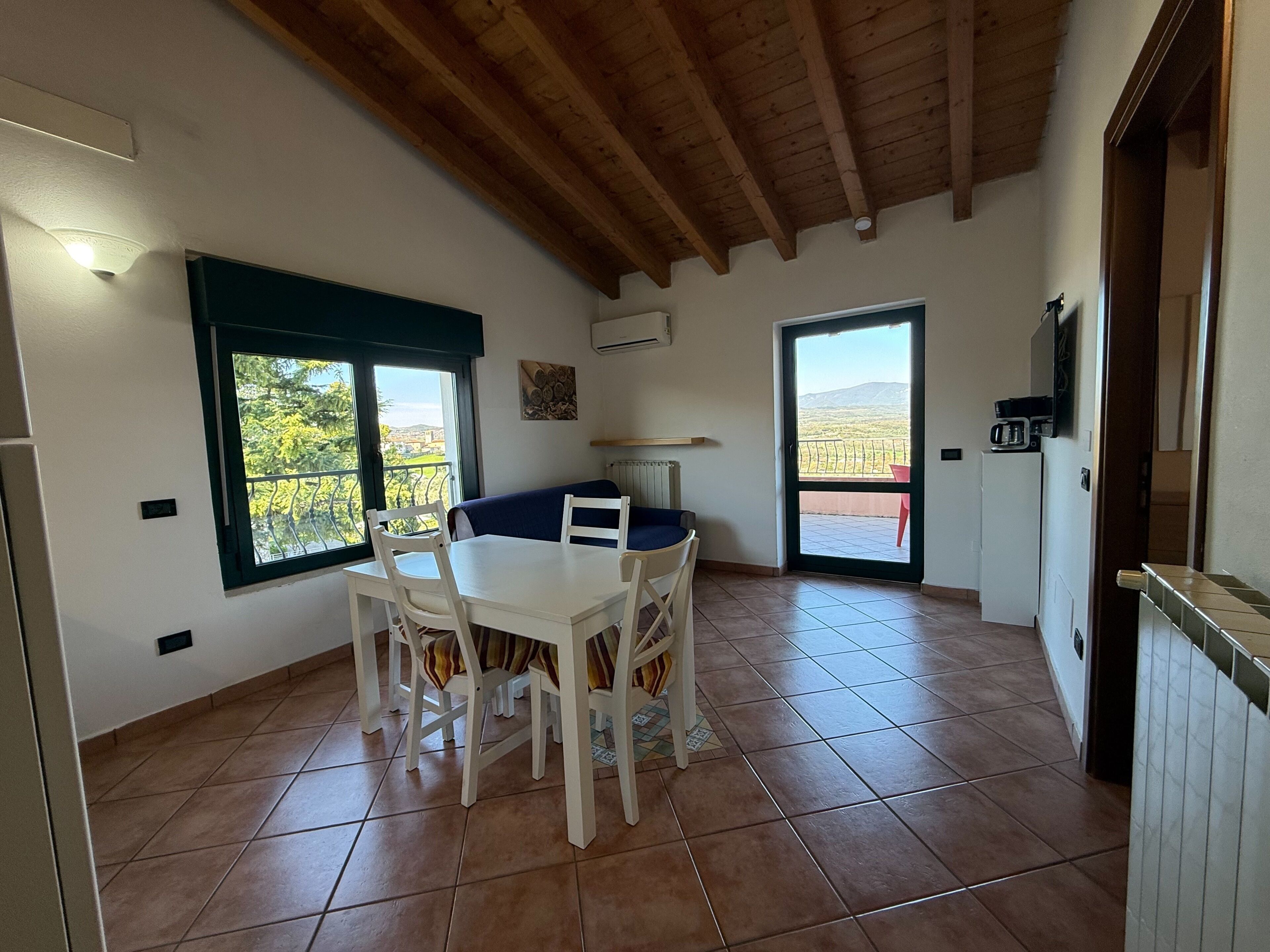 A dining area with a table and chairs, a window with a view, and a door leading to a balcony.