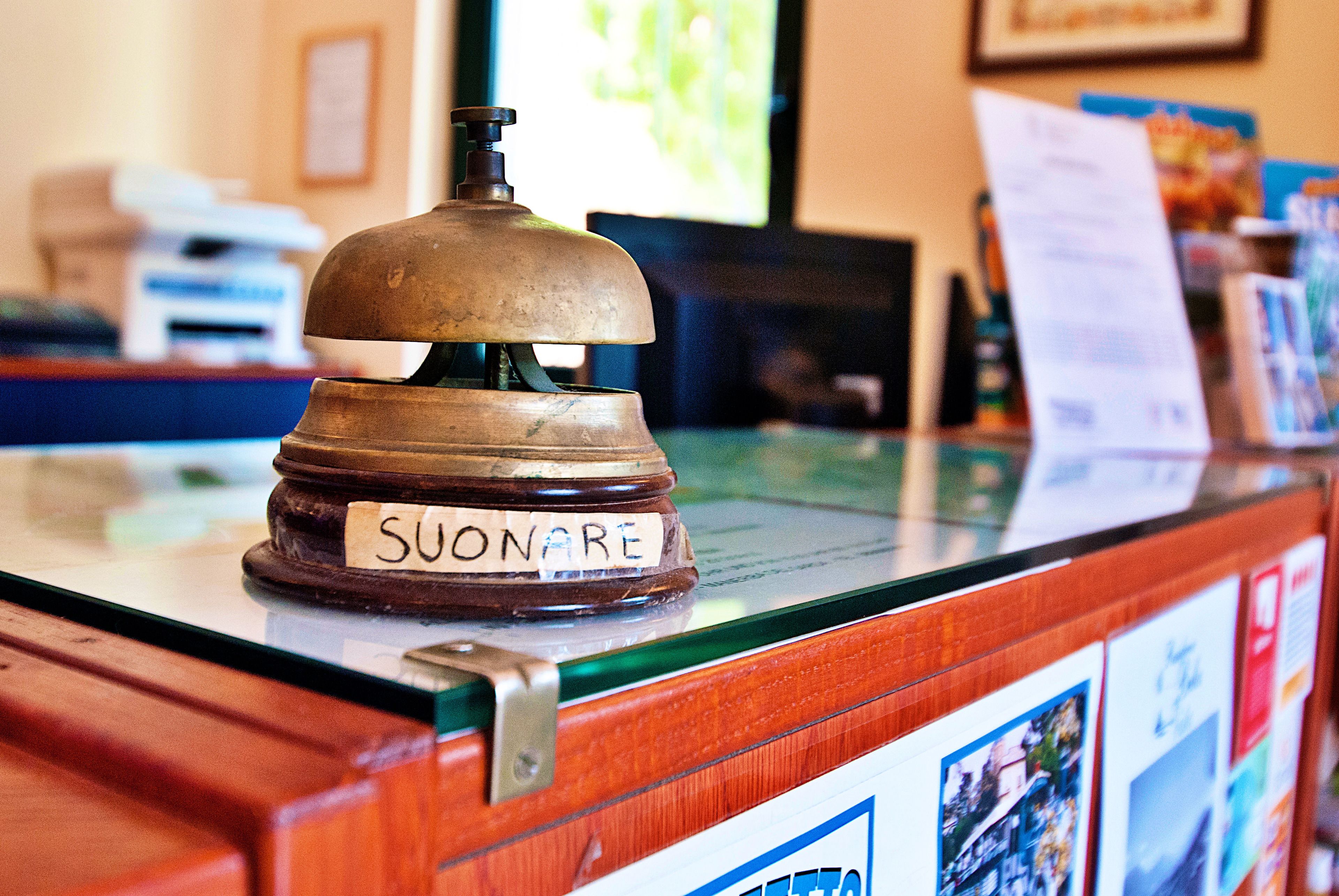 A wooden reception desk with a brass bell labeled "SUONARE" and a glass display case.
