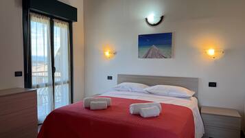 A hotel room with a bed, a nightstand, a dresser, a window with curtains, and a wall-mounted picture.