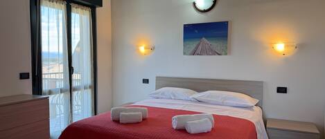 A hotel room with a bed, a nightstand, a dresser, a window with curtains, and a wall-mounted picture.
