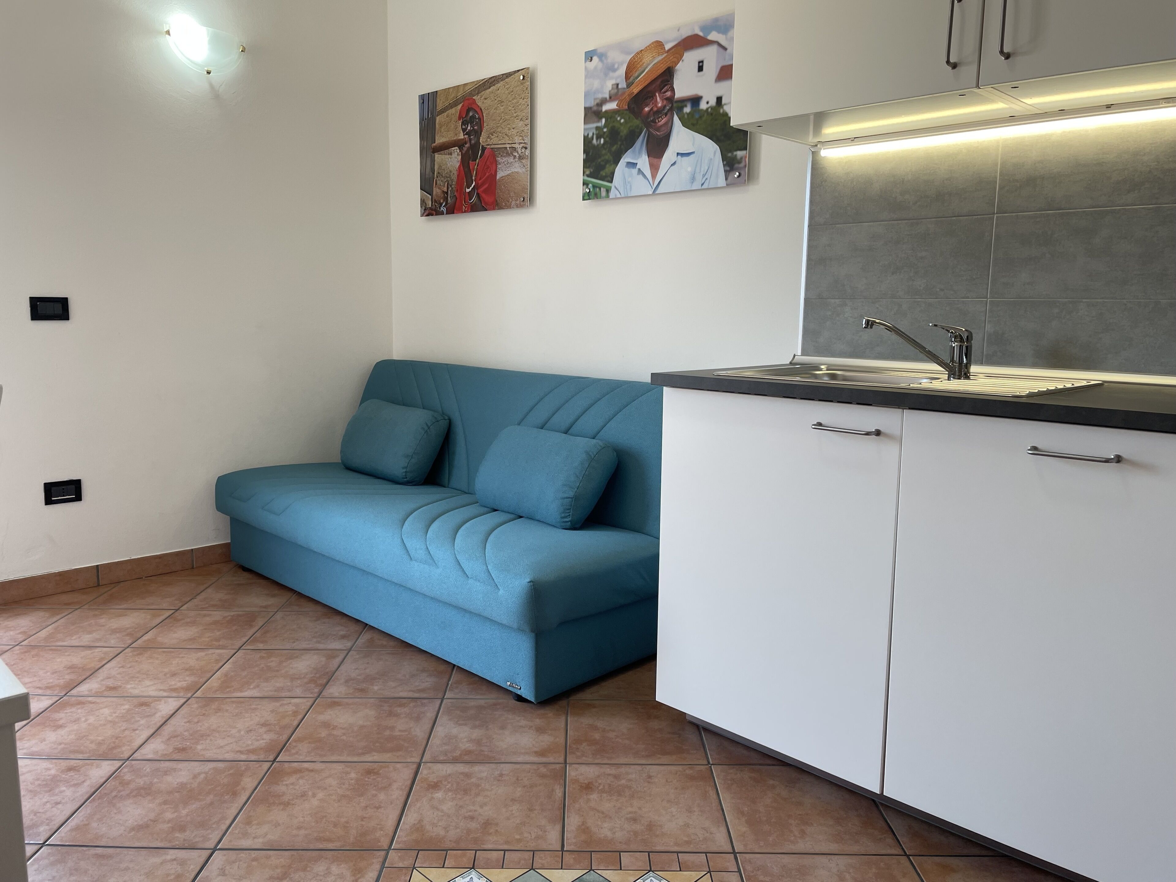 Eine kleine Küche mit Spüle, weißen Schränken und einem blauen Sofa mit Kissen.