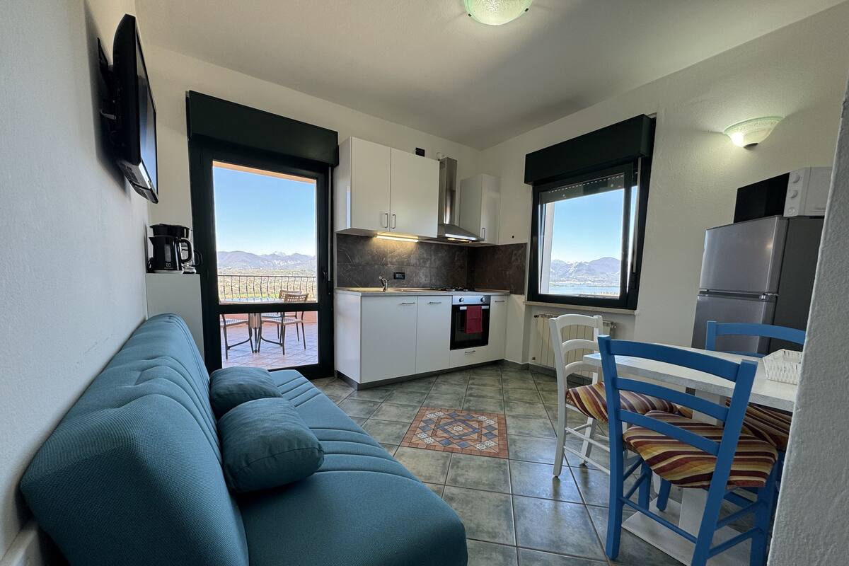 A compact living space with a sofa, dining table, chairs, a kitchen area, and a view of the mountains.