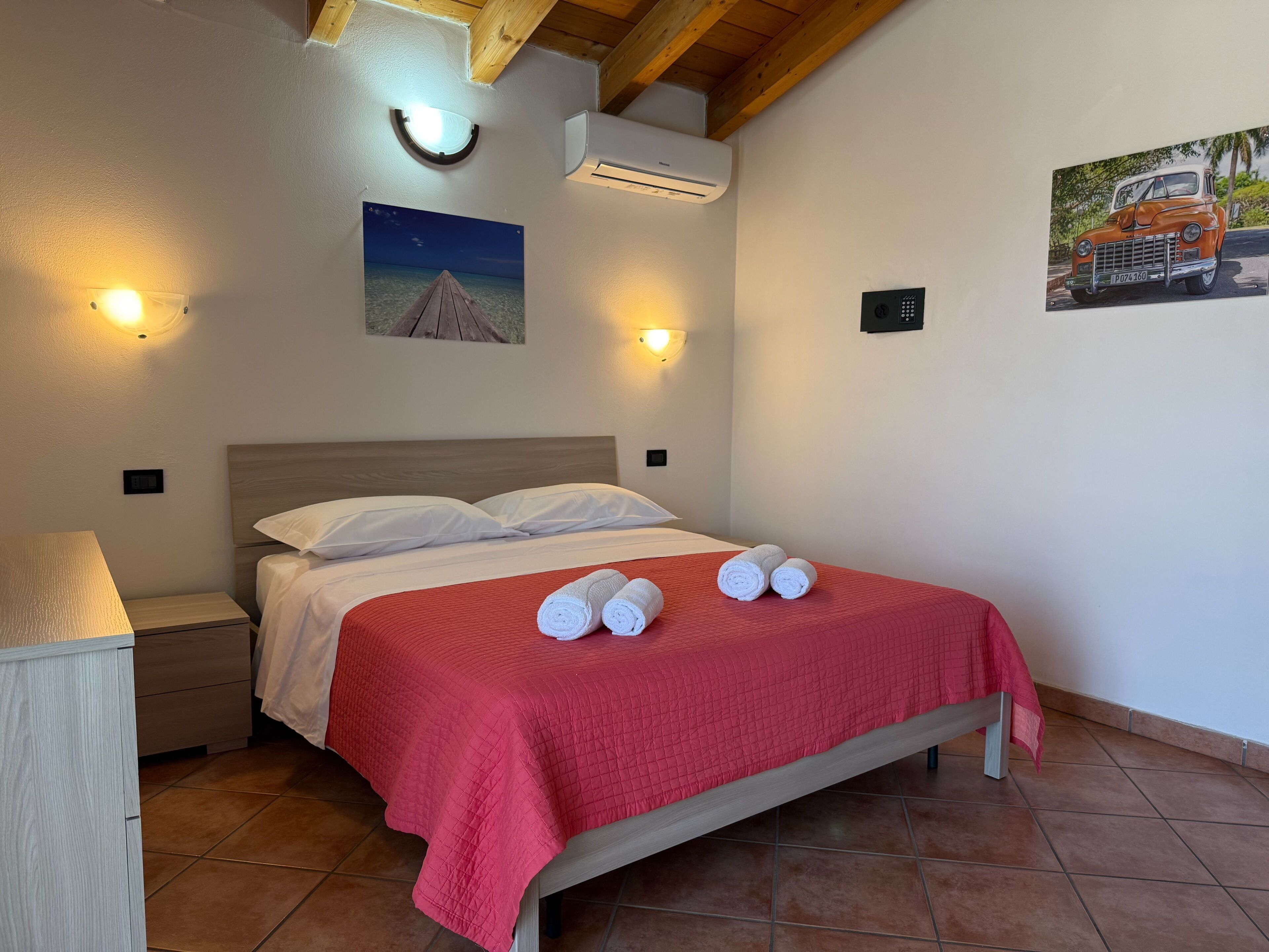Ein Schlafzimmer mit einem Bett, einem Nachttisch, einer Lampe, einer Wandklimaanlage und einem Gemälde.