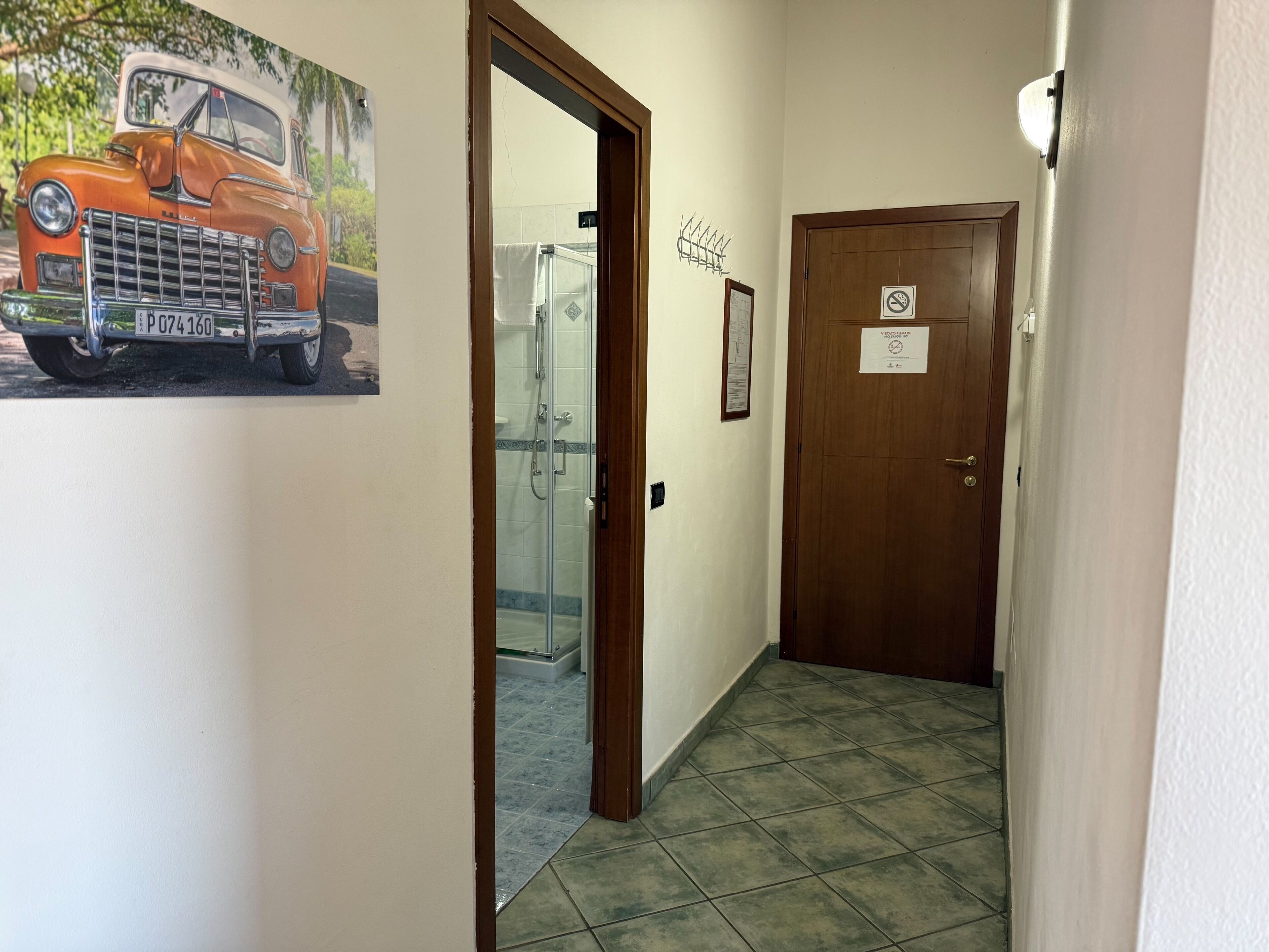 Un pasillo con una puerta de madera, una puerta de cristal para la ducha y un aplique de pared.