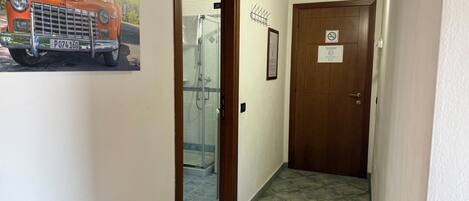 Un pasillo con una puerta de madera, una puerta de cristal para la ducha y un aplique de pared.