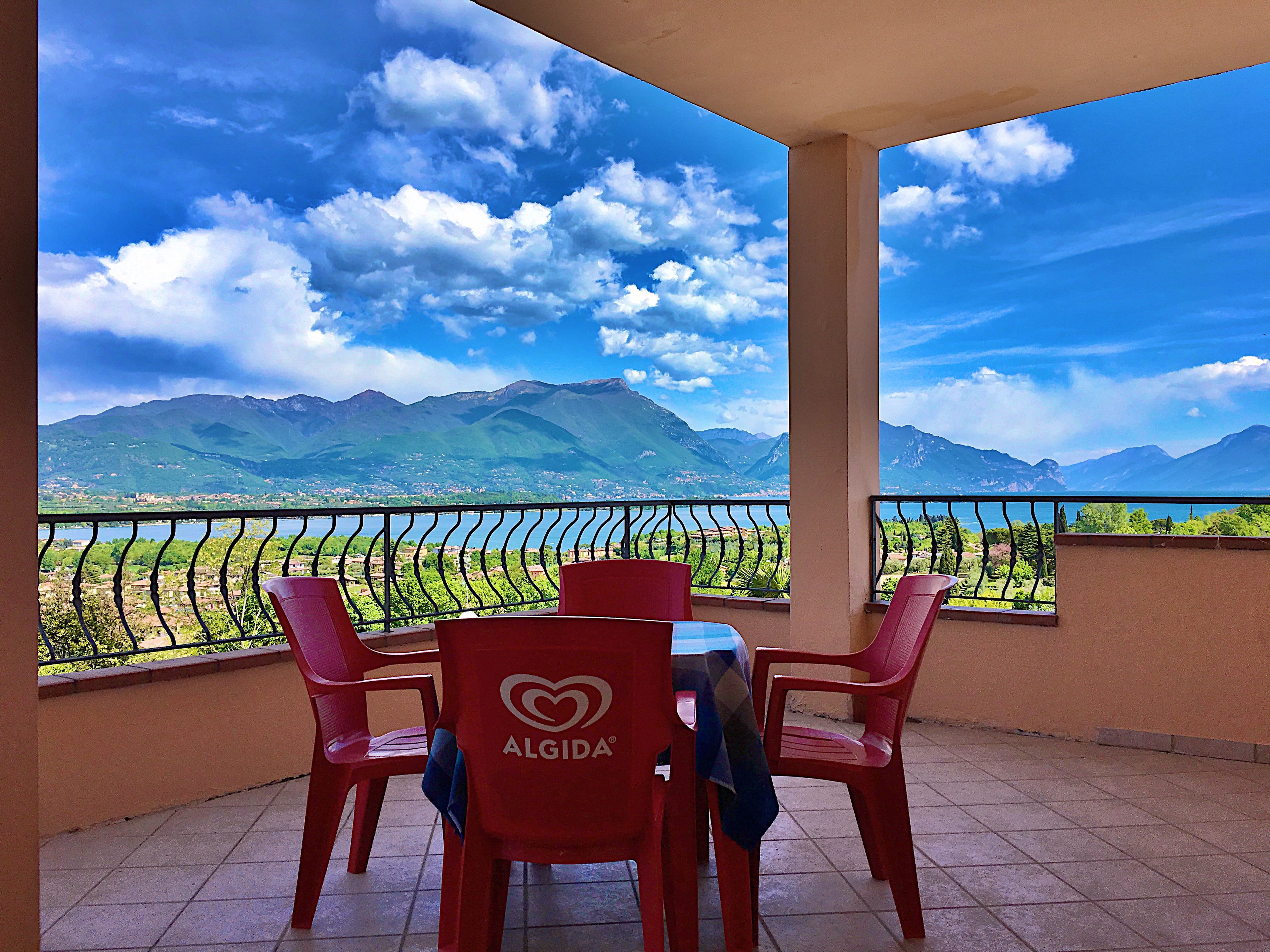 Un balcón con mesa y sillas, con vistas a un paisaje montañoso bajo un cielo despejado.