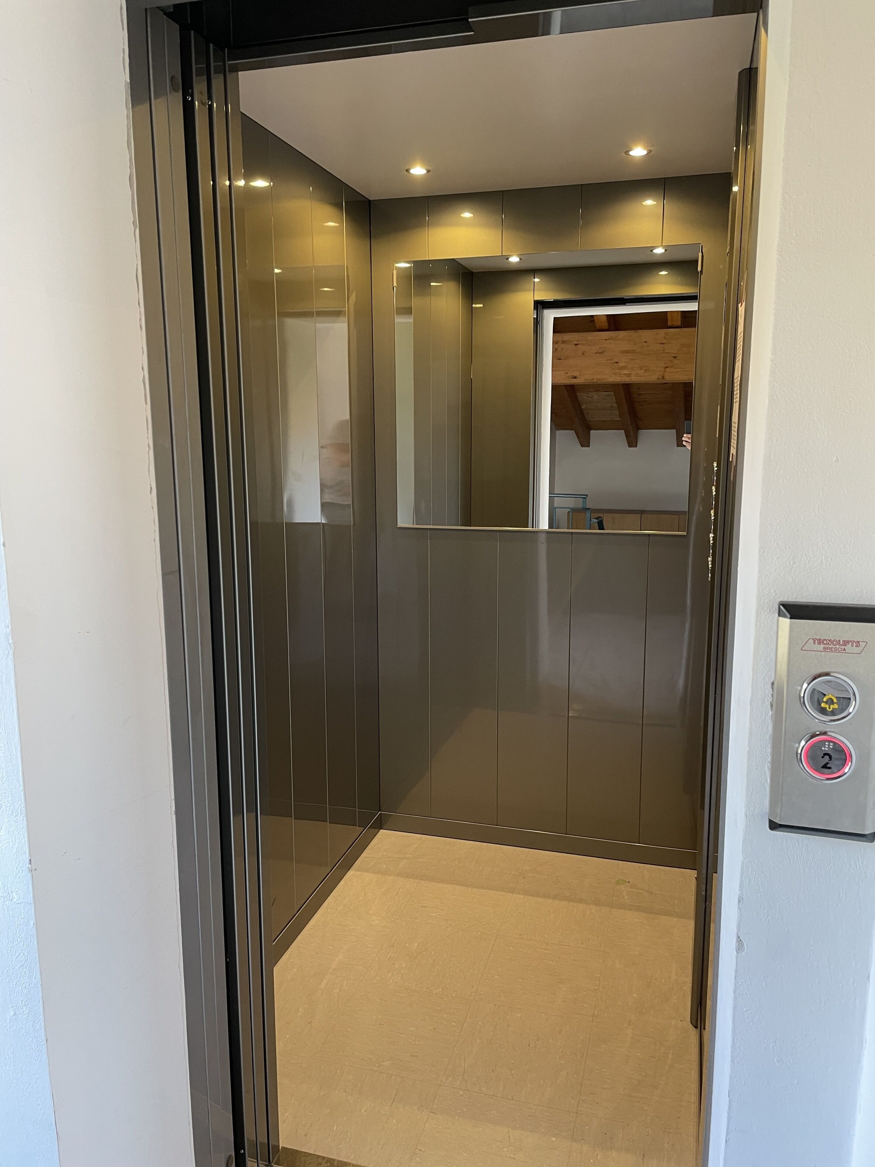 A modern elevator with metallic walls and a control panel on the right.
