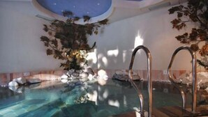 An indoor swimming pool with clear water, surrounded by rock formations and decorative foliage. - AlpHotel Taller (Dimaro Folgarida)