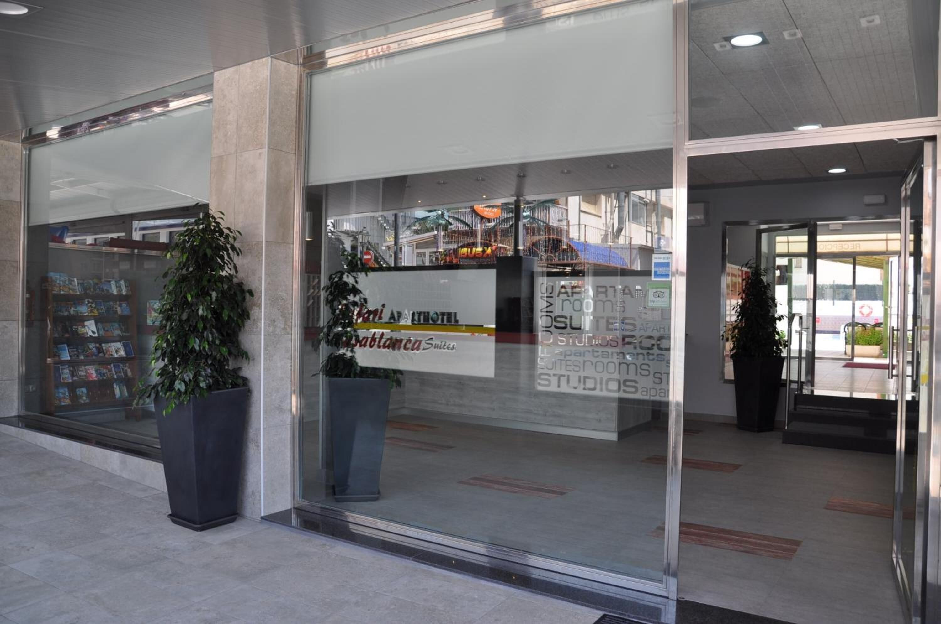 Entrada de hotel con fachada de vidrio, una planta en maceta y un letrero que dice 'Habitatia Suites'.