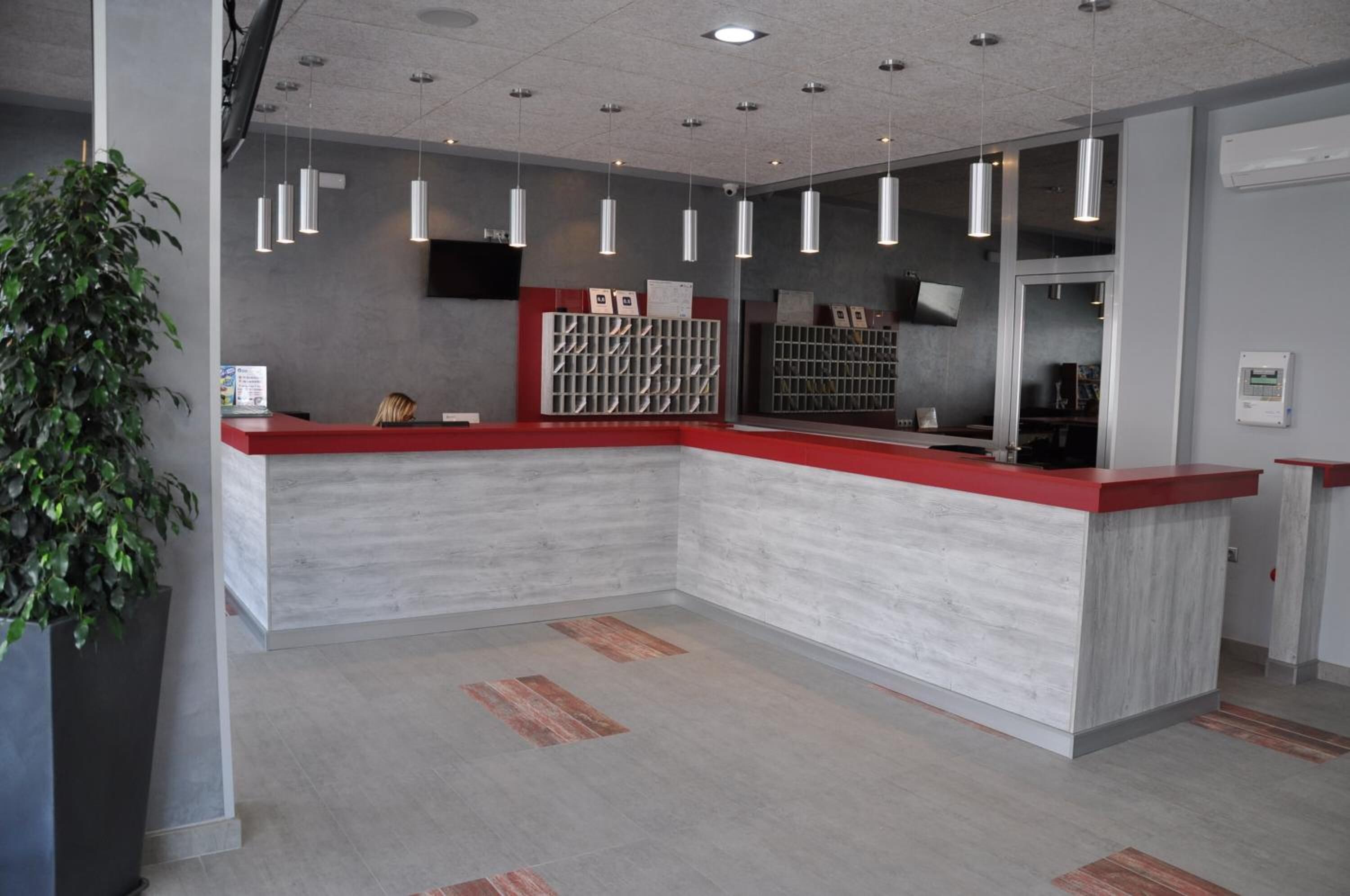 A reception area with a red counter, a plant, and a wall-mounted display.