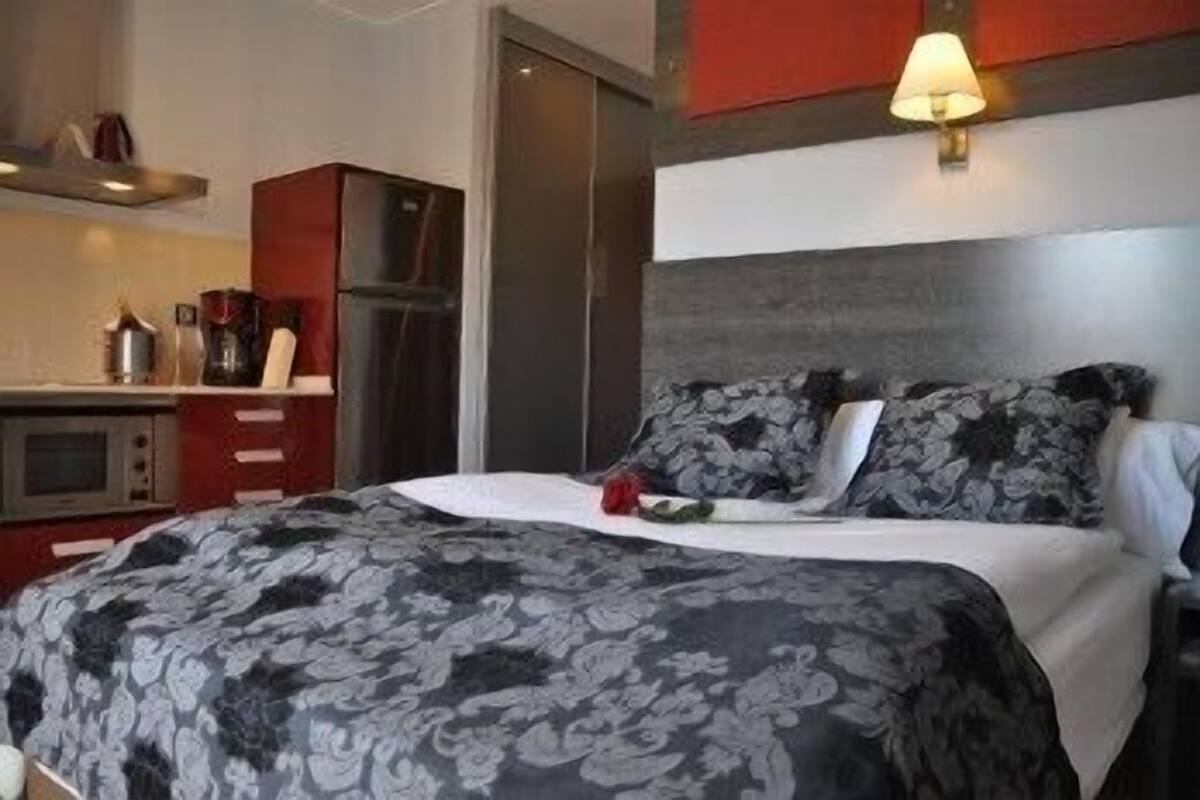 A hotel room with a bed, a small kitchenette, and a red accent wall.