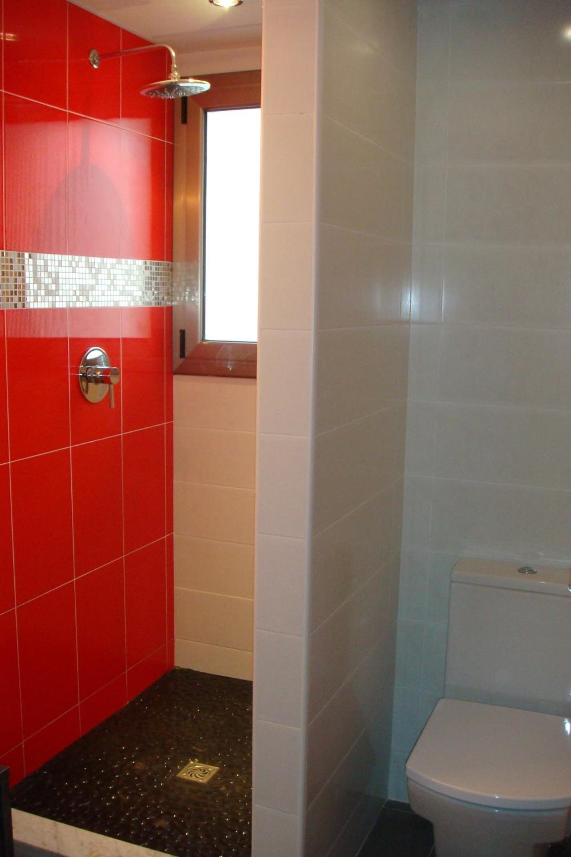A bathroom with red tiled walls, a white toilet, and a shower area.