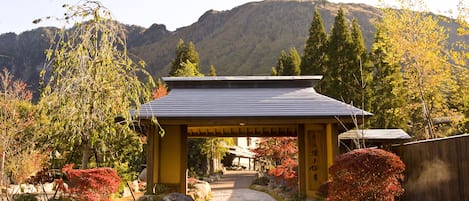 A traditional Japanese building with a tiled roof, surrounded by rocks and trees with autumn foliage.