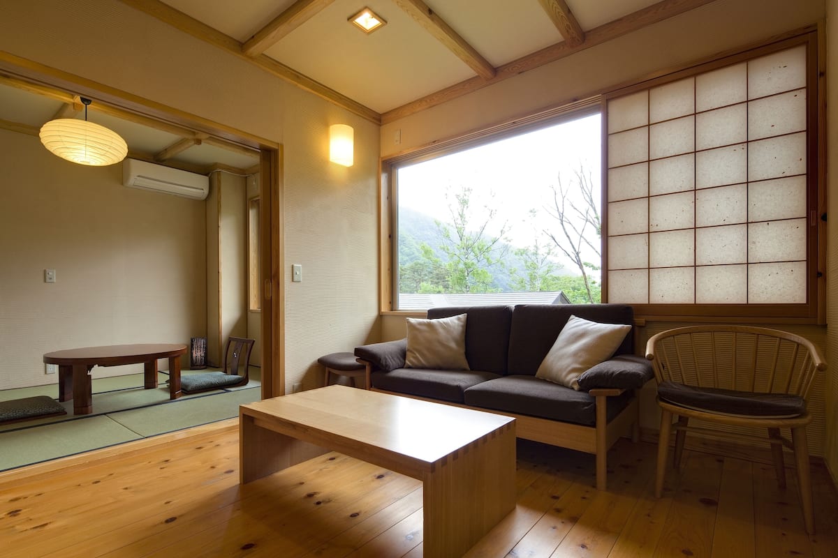A traditional Japanese-style room with tatami flooring, a low wooden table, a sofa, and a chair.