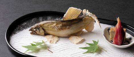 A dish with a fish, garnished with leaves and sugar, on a textured plate.