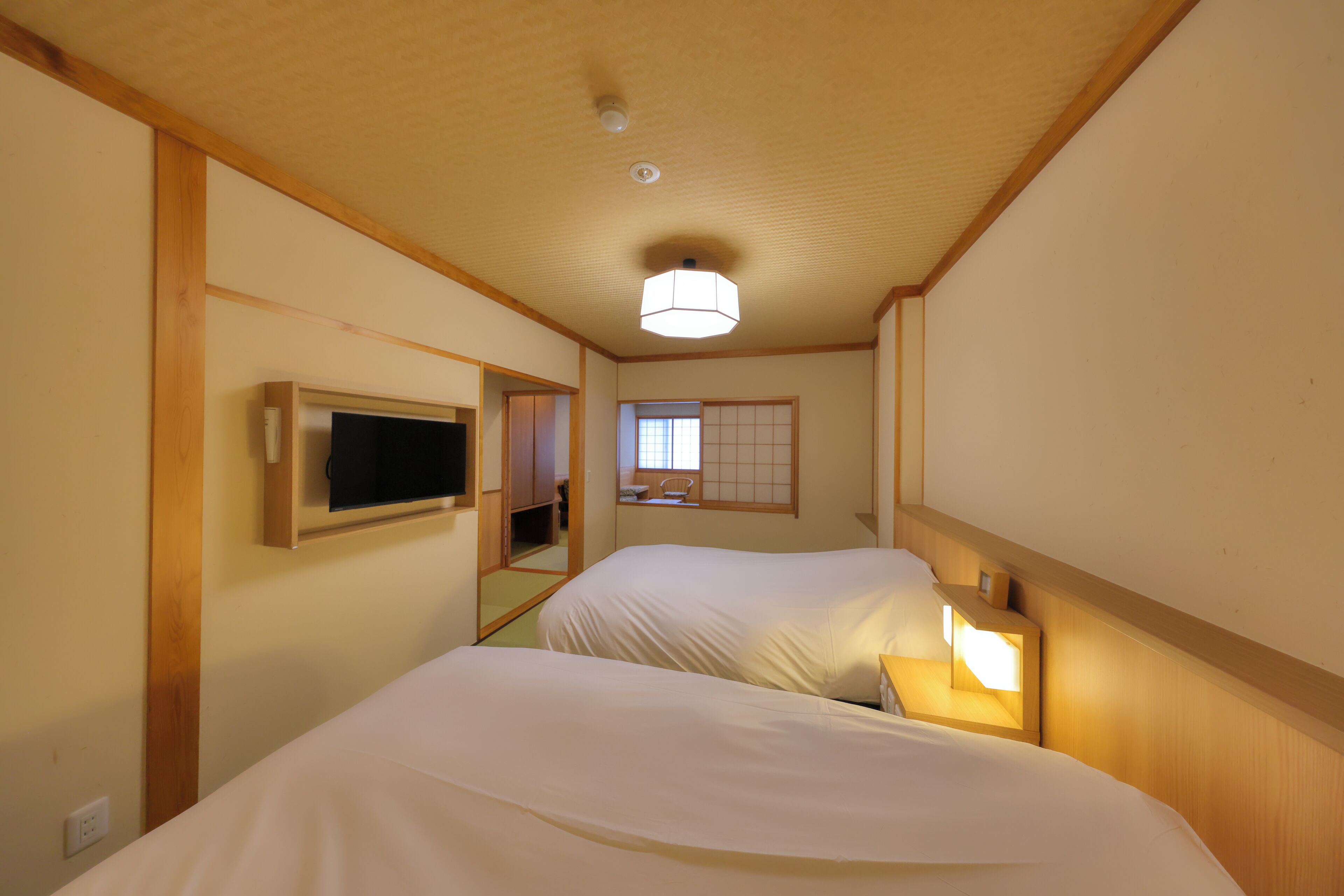 A hotel room with two beds, a television, a window with a view, and a ceiling light.