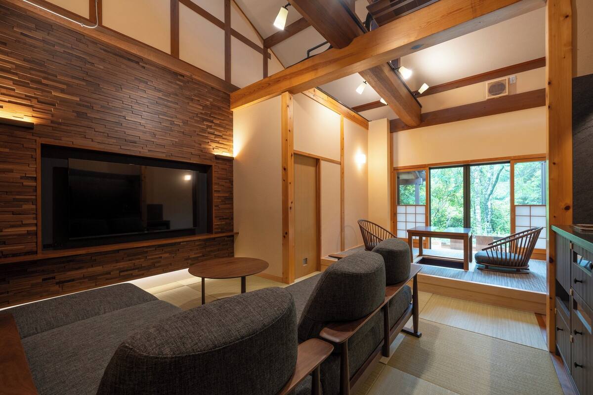 A modern interior with a wooden wall, a flat-screen TV, grey upholstered seating, and large windows.