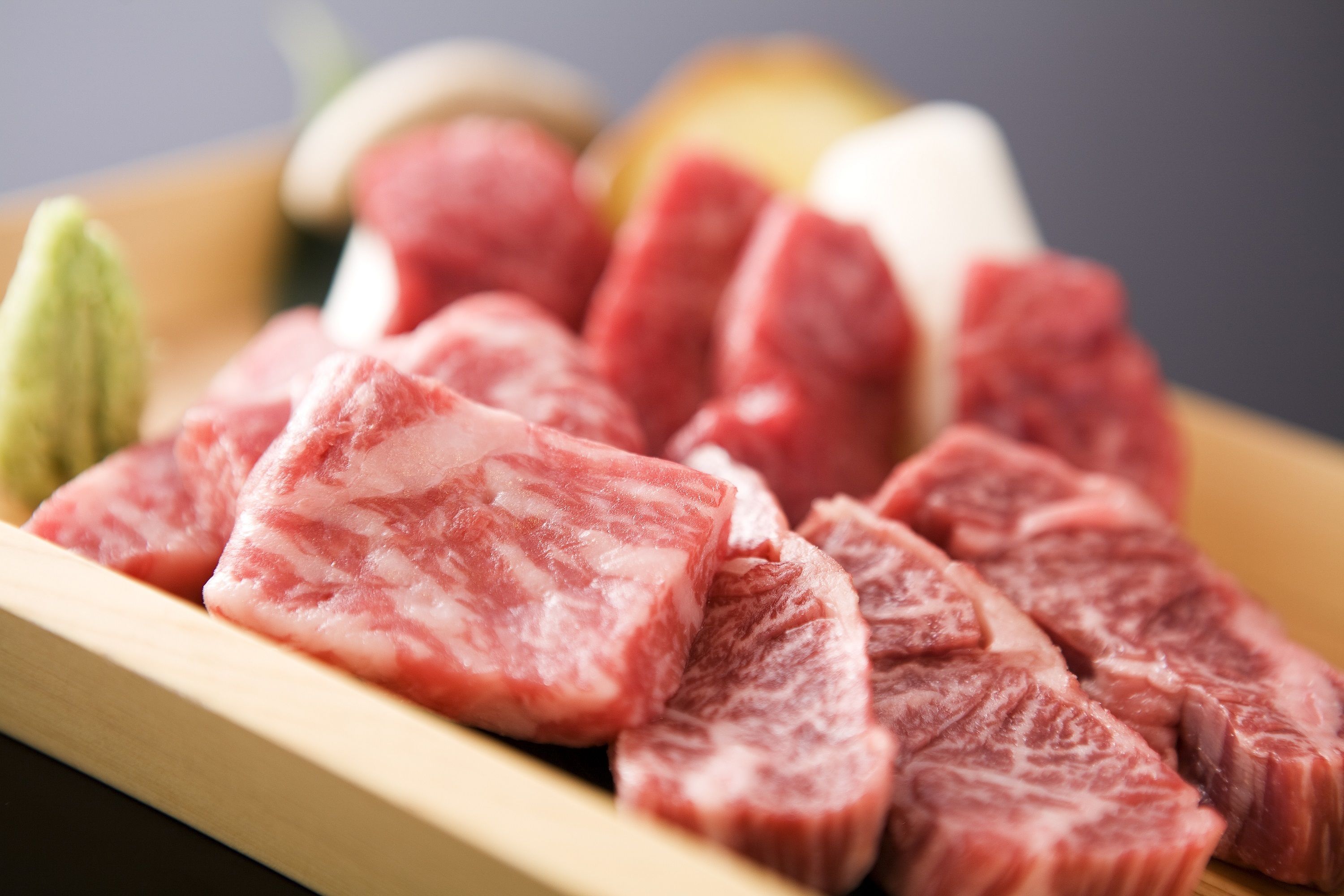 A wooden cutting board with raw meat and vegetables.