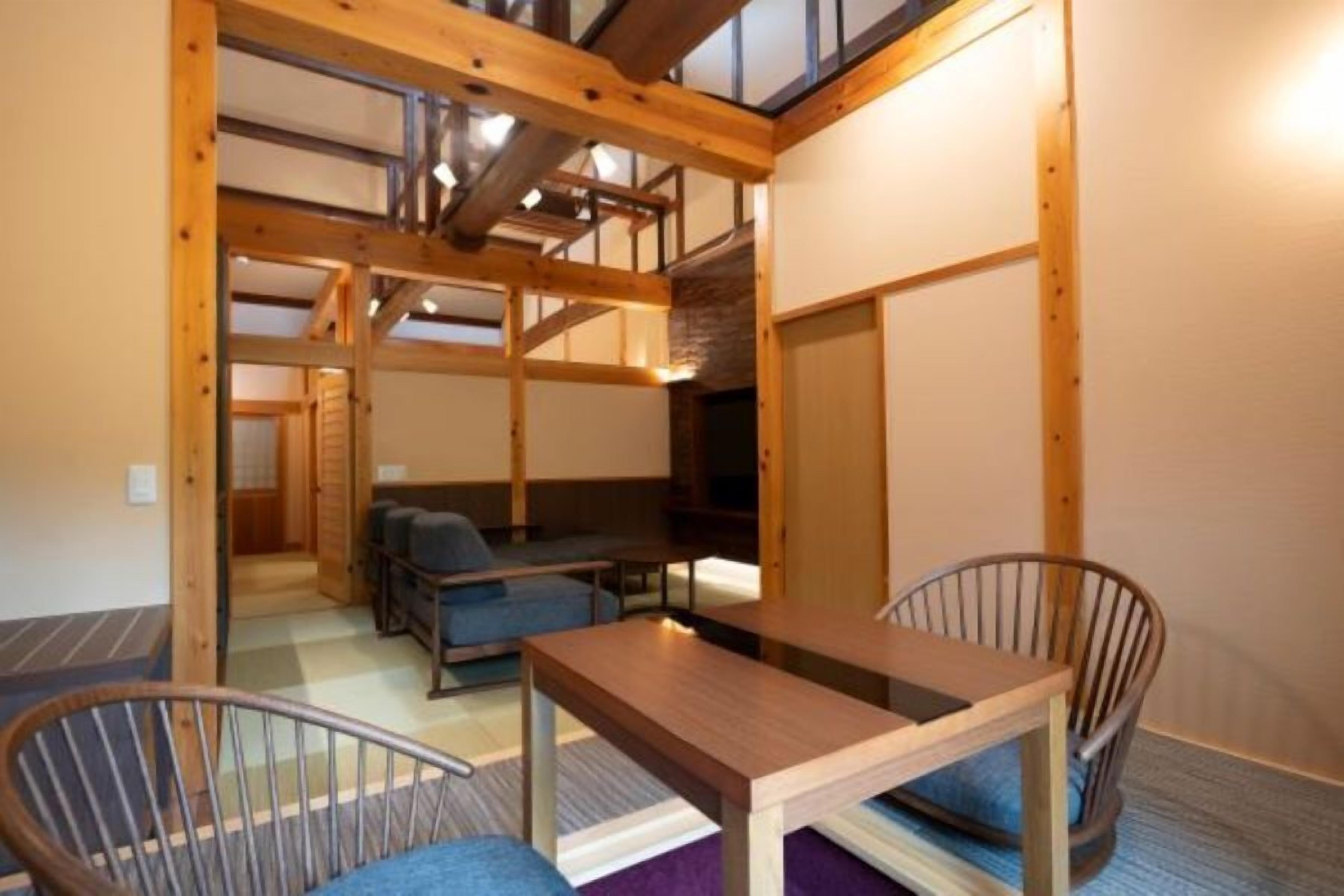 A room with a wooden ceiling, a table, two chairs, and a sofa.