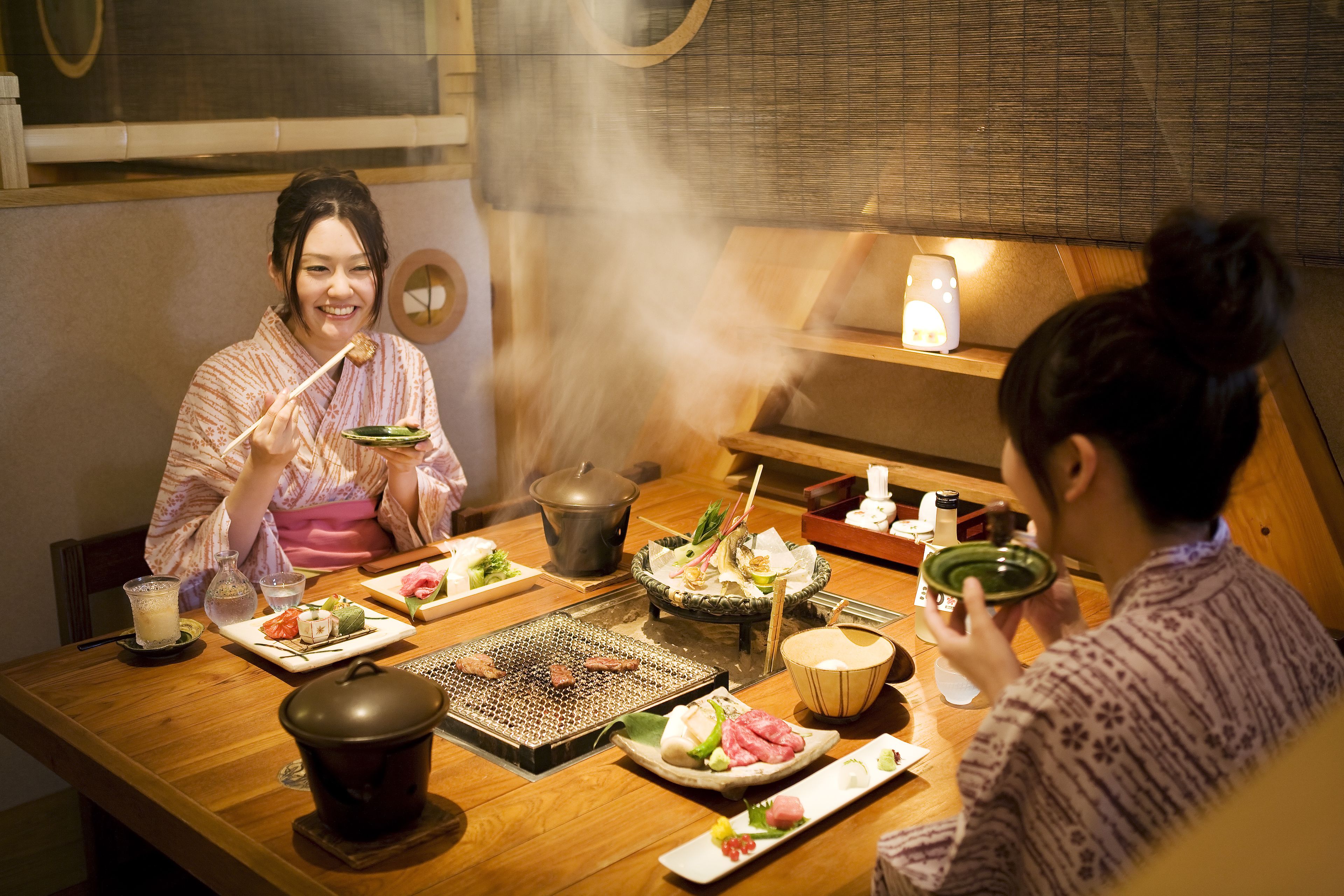 Une table à manger avec différents plats et un gril, de la vapeur s’élevant du gril, et une casserole posée sur la table.