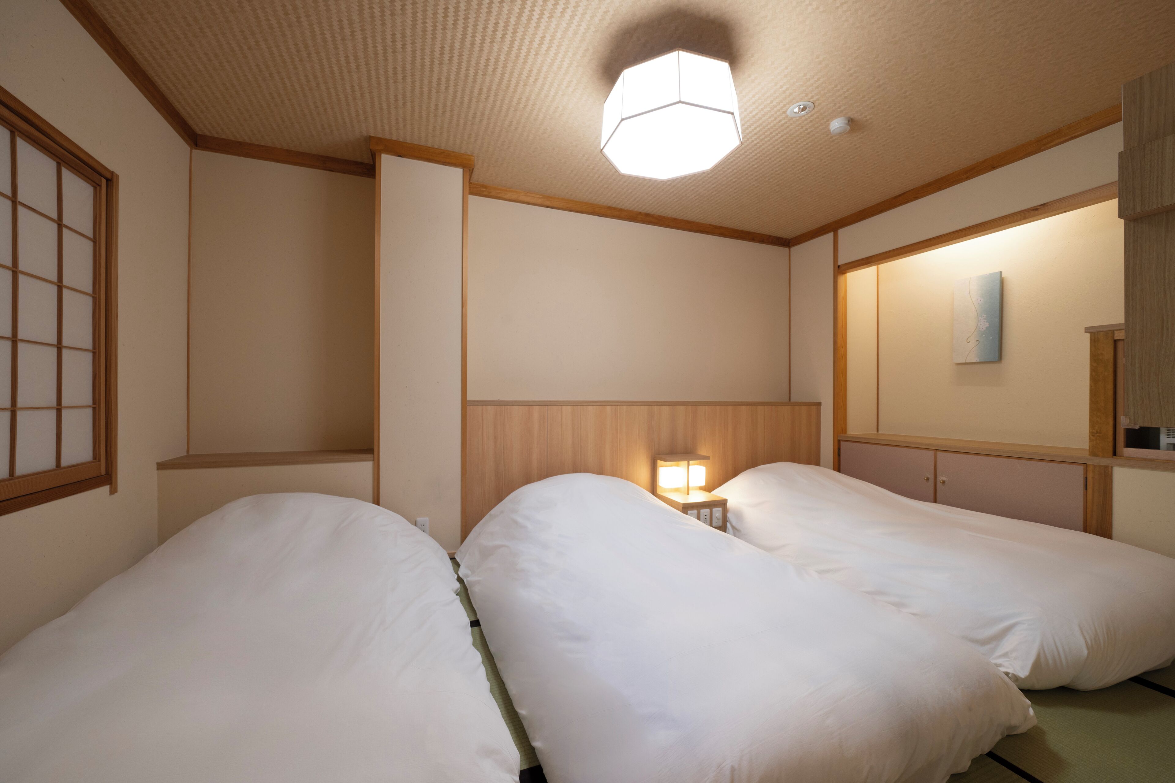 A hotel room with two beds, a wooden headboard, a nightstand with a lamp, and a wall-mounted artwork.