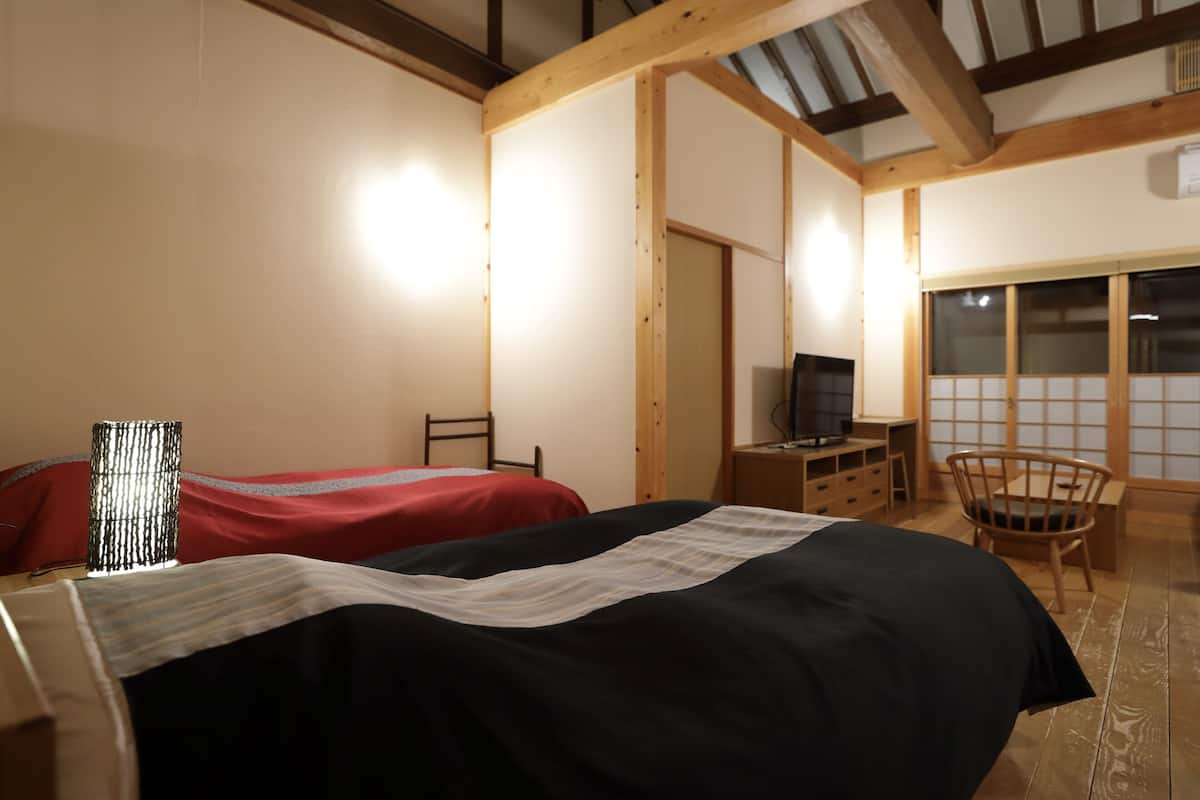 A room with two beds, a TV, a wooden desk, and a chair.