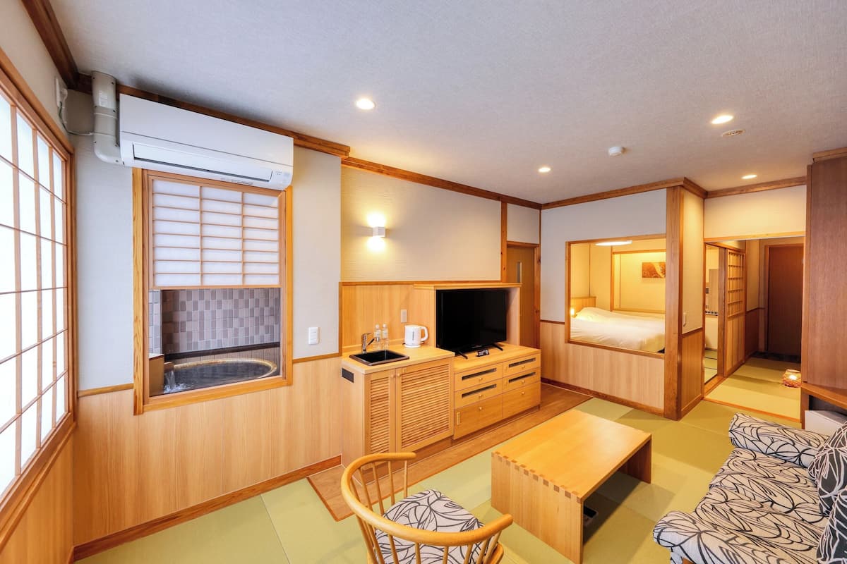 A traditional Japanese-style room with tatami flooring, a futon bed, a television, a sink, and a wooden cabinet.
