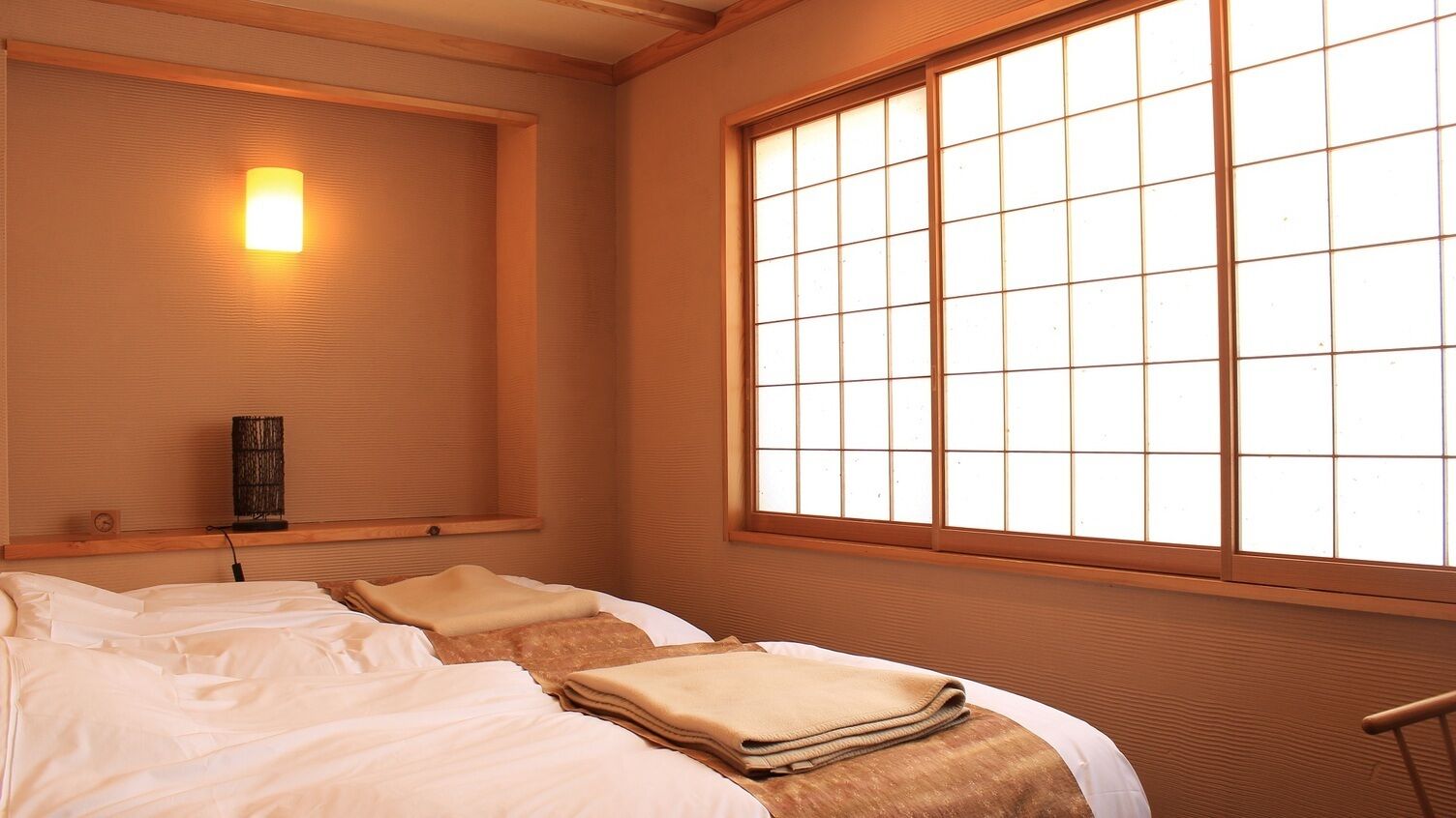 Une pièce avec un lit, une fenêtre à carreaux, une lampe fixée au mur et une étagère sur laquelle se trouve une autre lampe.