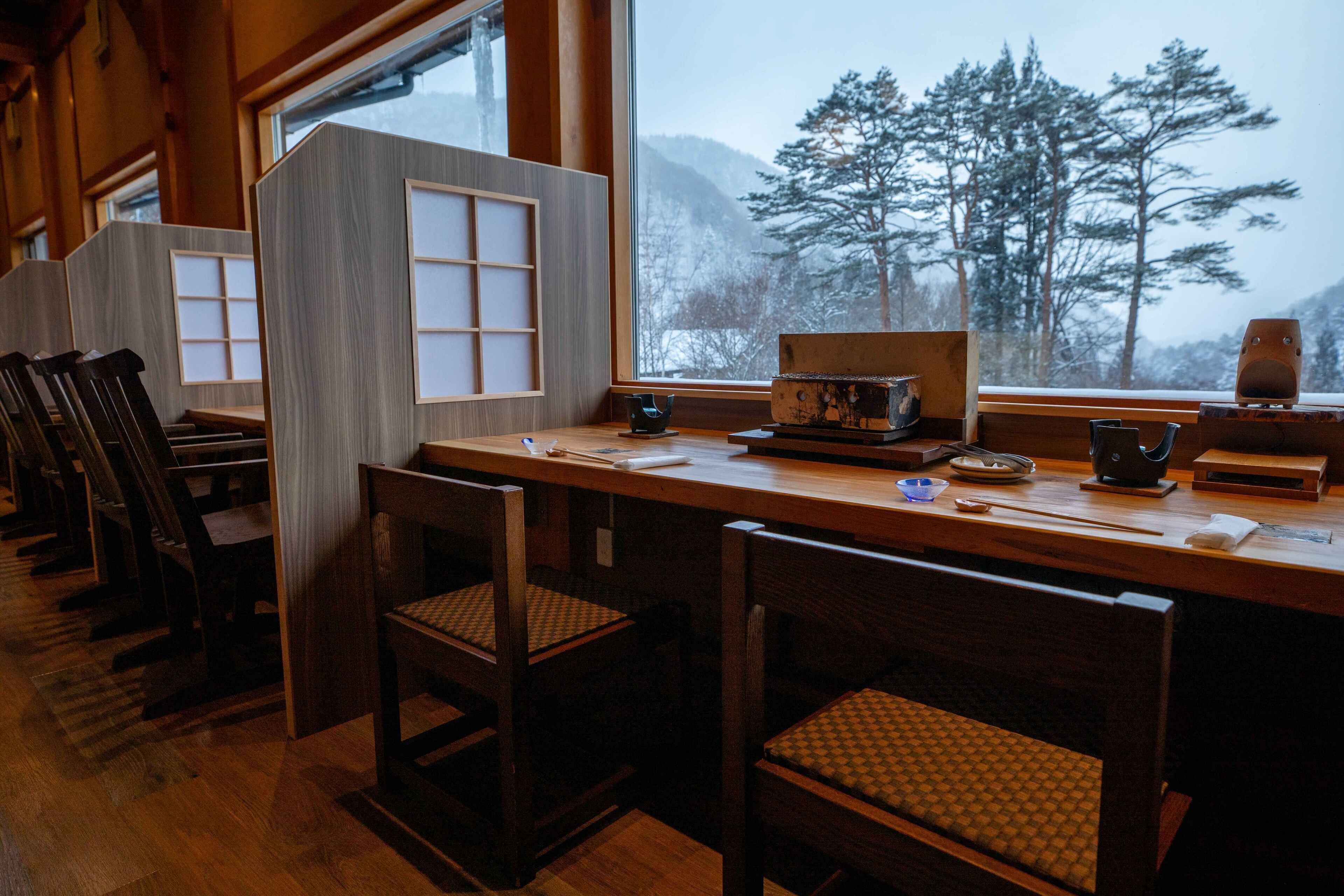 A traditional Japanese-style restaurant with wooden furniture and a view of snow-covered trees through large windows.