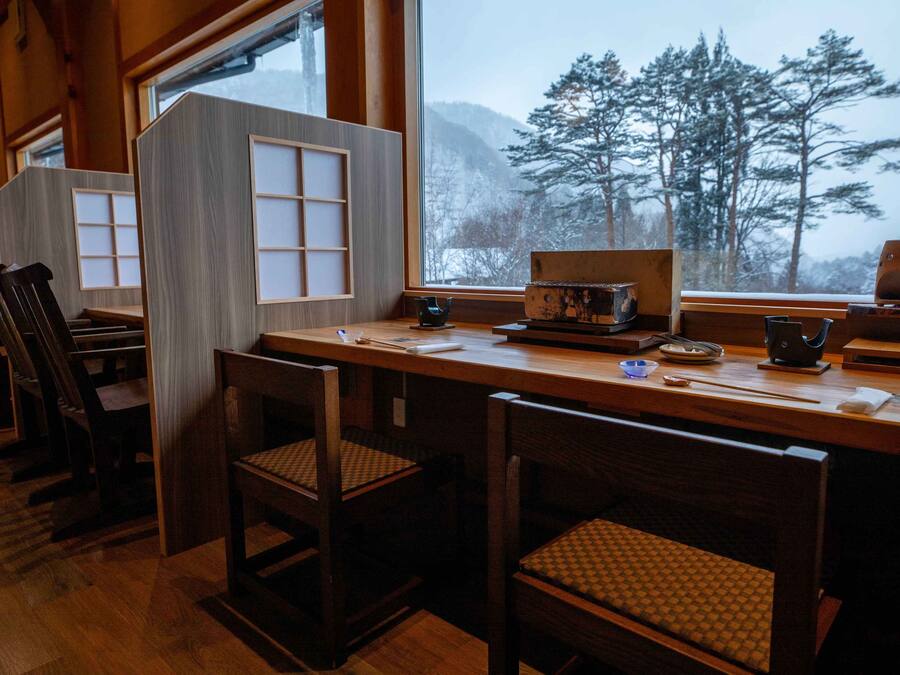 A traditional Japanese-style restaurant with wooden furniture and a view of snow-covered trees through large windows.
