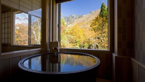 Una habitación con una bañera de madera, ventanas amplias y vistas a follaje otoñal y montañas.