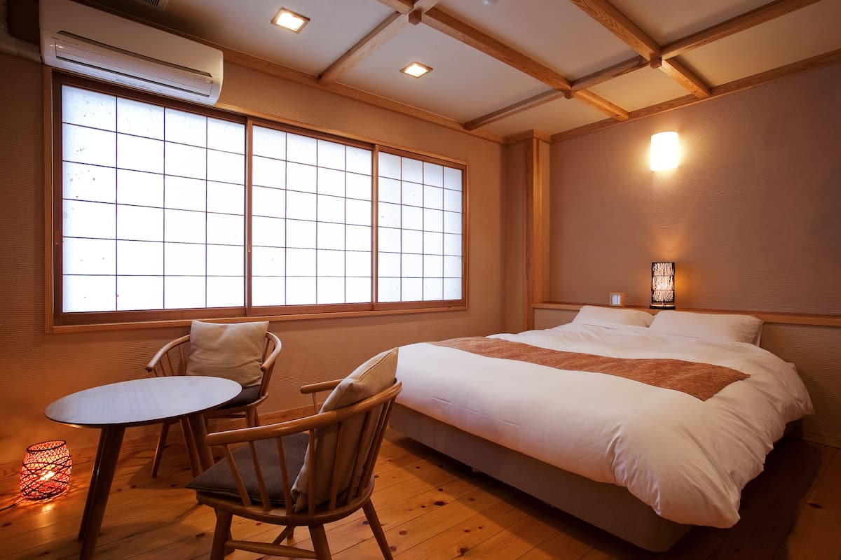 A room with a bed, a chair, a table, and a window with a view.