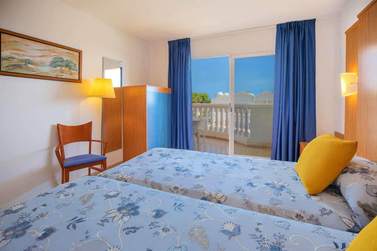 Ein Hotelzimmer mit Bett, Sessel, Schreibtisch und einem Balkon mit Vorhängen.